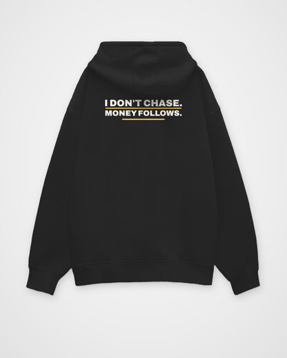 Black oversized hoodie, back view, print reading I don't chase. Money follows – digital mockup