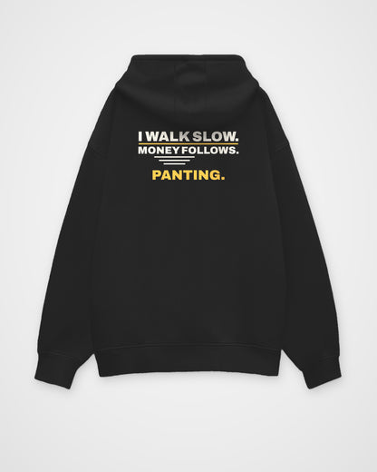 Black oversized hoodie, back view, print reading I walk slow. Money follows. Panting – digital mockup