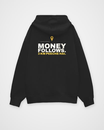 Black oversized hoodie, back view, print reading Money follows. 3 km peeche hai – digital mockup