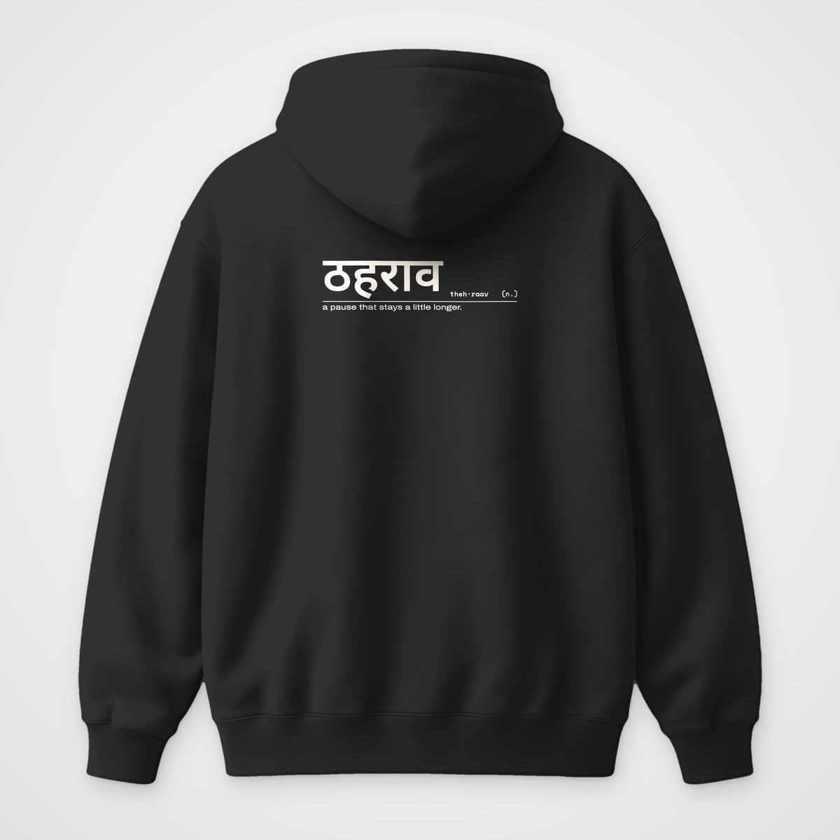 Black oversized hoodie, back view, with a small Hindi dictionary entry for ठहराव below the hood